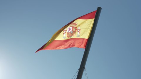 Spanish national flag blowing in the wind against a clear blue sky.