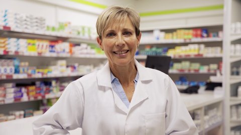 Female pharmacist standing smiling leaning happily against counter in pharmacy 