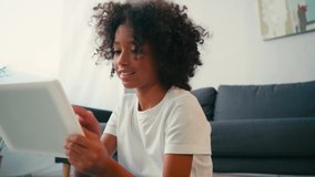 African american girl with crossed legs using digital while sitting near couch