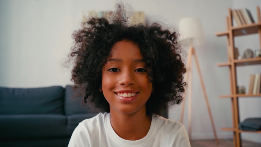 Selective focus of smiling african american girl looking at camera at home Royalty-Free Stock Footage #1060723066