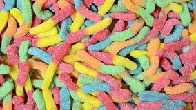 HD video zooming out from many colorful gummy worms coated in sugar, young caucasian female hand reaches in to remove a single gummy worm candy.
