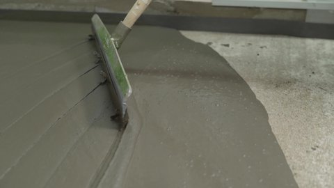 Self-leveling cement floor. Leveling the floors with a cement mixture. The process of leveling the mortar on the floor. The worker levels the self-filling liquid floor with a trowel. Leveling the