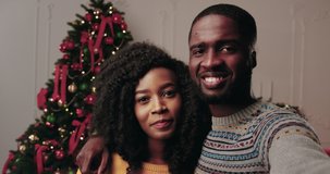 Portrait of happy African American young family on Christmas tree background. Two people smiling and hugging record video greeting. Camera view.