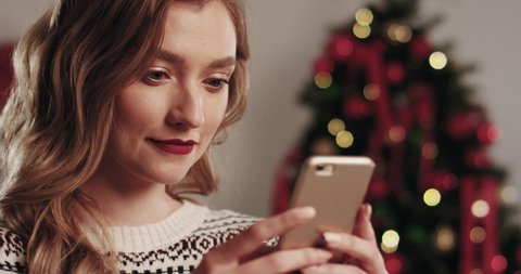 Portrait of young beautiful blonde woman in winter sweater typing message on mobile phone and reacting emotionally receiving good news.