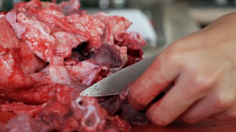Human hands use a butcher's knife, which is used to cook and cut meat. Hands with a knife cut meat, pork covered in blood