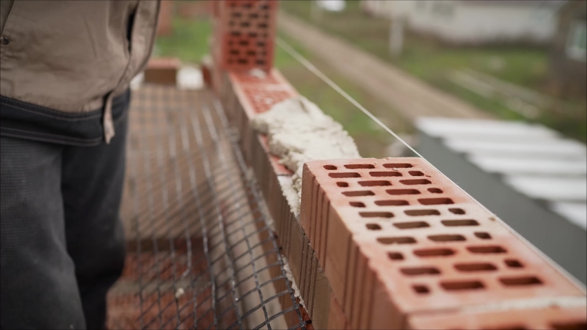 A master mason is laying a red brick wall. The master at the construction site is laying a brick laying. master bricklayer building-up one family house Royalty-Free Stock Footage #1060736638