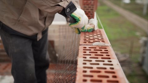 A master mason is laying a red brick wall. The master at the construction site is laying a brick laying. master bricklayer building-up one family house