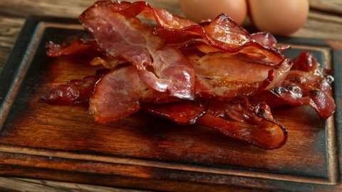 Super Slow Motion Shot of Roasted Bacon Slices Falling on Wooden Board at 1000 fps.