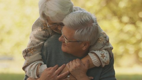 Happy old couple hugging in park. Senior man flirting with elderly woman. Romance at old age dancing on autumn day. High quality 4k footage