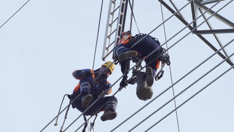 Two maintenance technicians sit high up on power lines