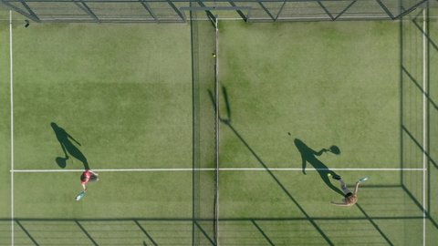 Aerial, top down, drone shot, rising above people playing tennis. 
Two girls play padl tennis