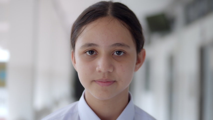 Slow motion of a smiling high school teen girl in white uniform student is greeting by facial expression happily.
