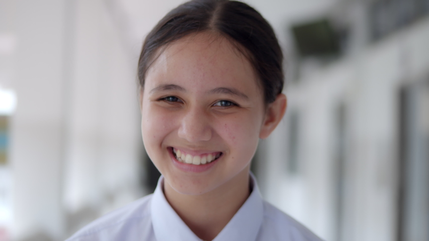Slow motion of a smiling high school teen girl in white uniform student is greeting by facial expression happily.