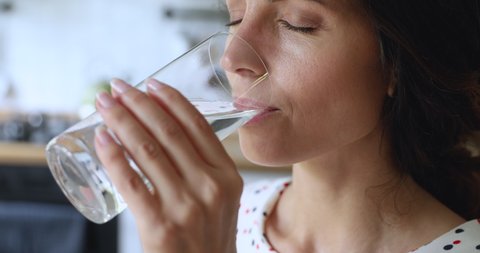 Close up view thirsty young woman holding glass make sip drinks still water enjoy natural aqua standing in home kitchen preventing organism dehydration, skin and health care, healthy lifestyle concept