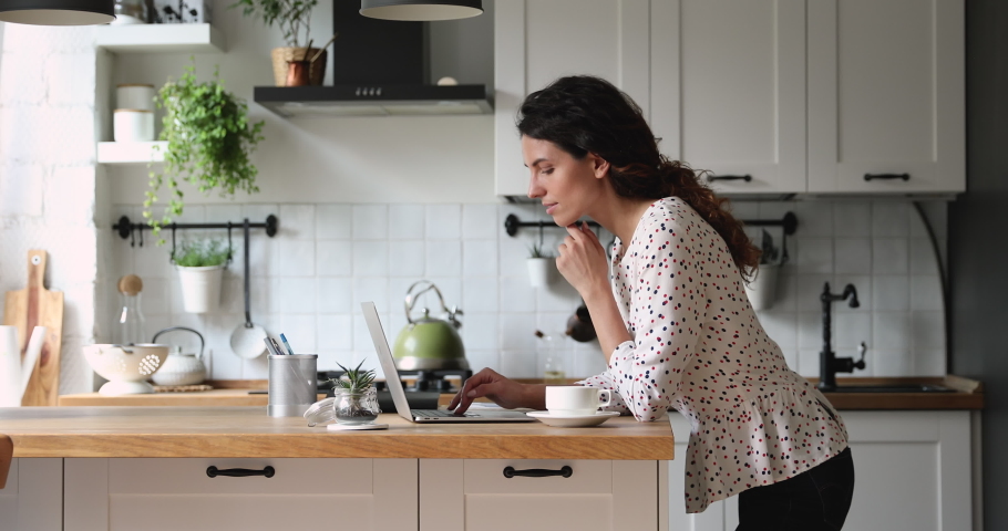 Woman standing in home cozy kitchen use laptop do freelance work looking focused deep lost in thoughts, thinking solving issues distantly makes research, author writing creative work online concept Royalty-Free Stock Footage #1060757575