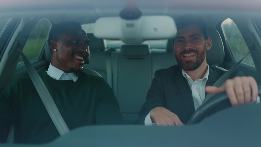 Funny two young mixed race men smiling sitting driving car at sunlight. Feel happy. Talking about business. Wheel automobile transport. Slow motion Royalty-Free Stock Footage #1060757659