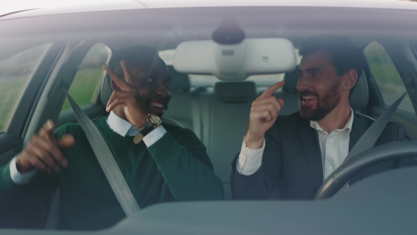 Two happy young attractive businessmen listening music dancing in car at sunlight. Feel happy. Talking about business. Wheel automobile transport. Slow motion Royalty-Free Stock Footage #1060757662