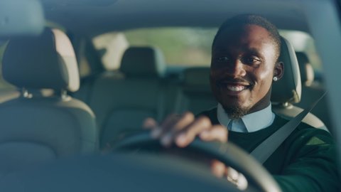 Funny young african american man smiling driving car with passenger. Feel happy at sunlight. Automobile businessman traffic transportation. Slow motion