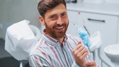 Cheerful millennial male patient talking with the dentist thankful for dental surgery smiling very happy showing healthy teeth. Oral hygiene. Stomatology.