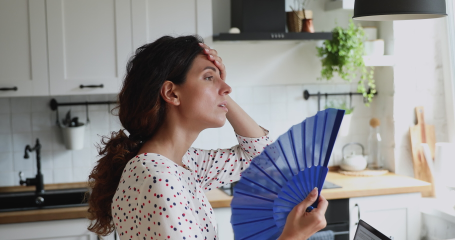 Overheated millennial 35s female standing in domestic kitchen using handheld blue waver, waves herself with hand fan suffers from hot weather indoor. Period, hormonal imbalance unhealthy woman concept | Shutterstock HD Video #1060760152