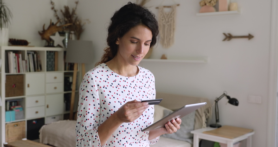 Millennial 35s woman standing in domestic room holding tablet portable device enter plastic credit card number makes secure easy distant electronic payment. Pay for goods services on internet concept Royalty-Free Stock Footage #1060760176