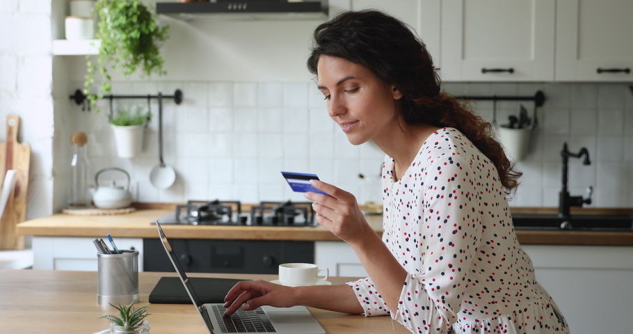 Housewife stands in domestic kitchen lean at dining table using laptop buy on internet by credit card. Good price great offer, enjoyment of e shopping, save money. Easy distant e-pay from home concept Royalty-Free Stock Footage #1060760179