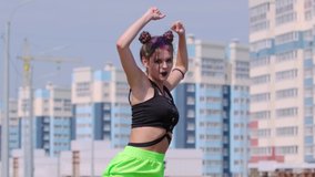 Video of an active young girl dancing hip hop outdoors on the background of high-rise buildings.