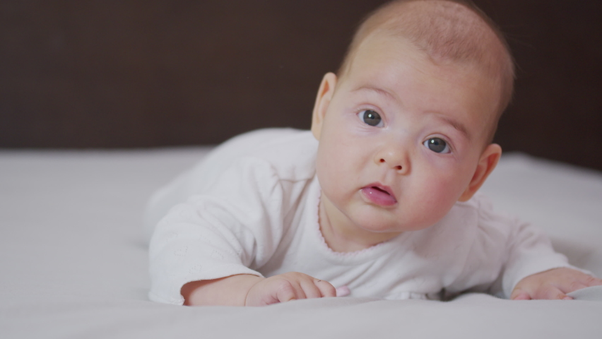 Beautiful Smiling Baby: A gorgeous little baby lies on the bed and smiles at the camera with a nice soft focus background. | Shutterstock HD Video #1060761463
