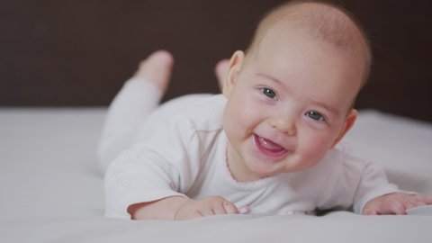 Beautiful Smiling Baby: A gorgeous little baby lies on the bed and smiles at the camera with a nice soft focus background.