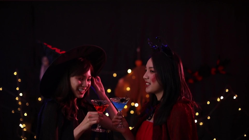 An Asian woman holding an alcoholic drink at a Halloween party.
