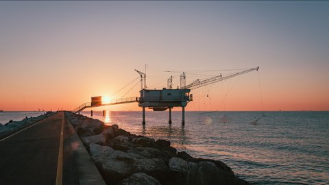 Marina di Ravenna / Italy - August 2020: Sun rising on the Zaccagnini pier in Marina di Ravenna with fishermen. Timelapse 4K