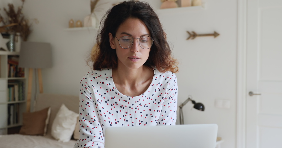 Beautiful young concentrated business woman wear glasses texting on laptop, thinks over issue, search solutions ideas, working home. Quarantine time, does business remotely using laptop and internet Royalty-Free Stock Footage #1060767064