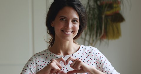 Pretty young woman volunteer pose indoor makes with fingers shape of heart smiling looking at camera. Symbol of I love you and thank you, charity sing, voluntary social work, organ donation concept