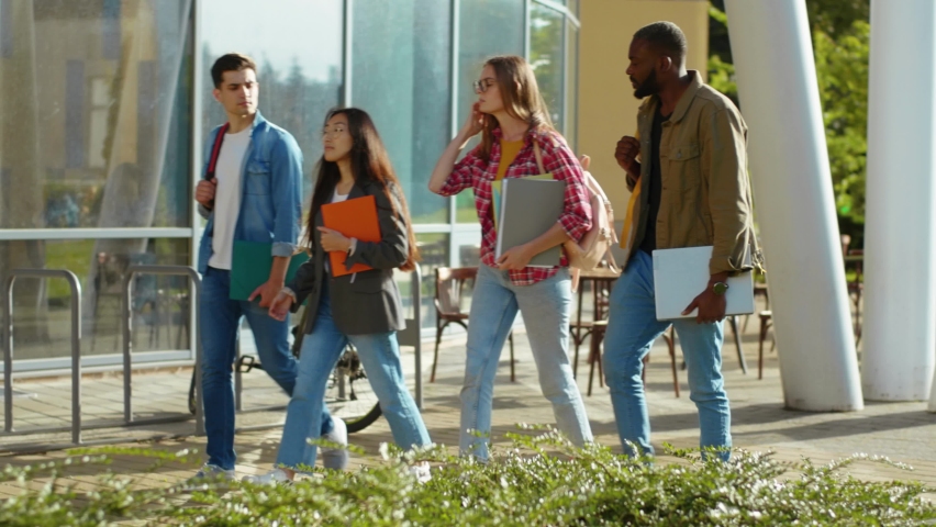 Four mixed-race young students walking on sunny street communicating sharing stories laughing enjoying funny company. Smart generation. Campus, university, education. | Shutterstock HD Video #1060767556