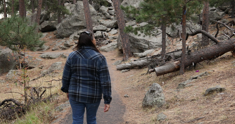 Woman hikes trail around Devils Tower Wyoming forest 4K. 1,267 feet tall igneous rock tower in Black Hills of South Dakota and Wyoming. United States National Monument. Recreation, tourism, vacation.