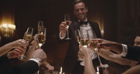 Handsome man making a toast with friends at party. Friends sitting at a table, toasting with wine and enjoying dinner together.
