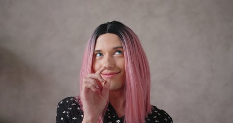 Positive young transwoman wearing black dot blouse and bright pink wig talks posing for camera on beige color background closeup