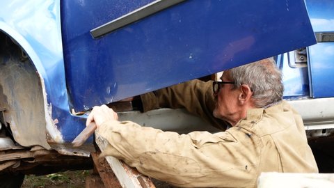 Car body repair on sill panel with hammer, Auto mechanic hammering old blue car door sill