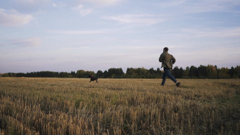Action shooting with a shaking camera. A young man runs across the field at sunset with her dog breed Kurtzhaar, happily shouting and playing catch-up.