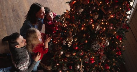 Full caucasian family couple and little cute children gathered near Christmas tree engaged in decorating it enjoy process preparing for New Year celebration, adorn house feels happy, view from above