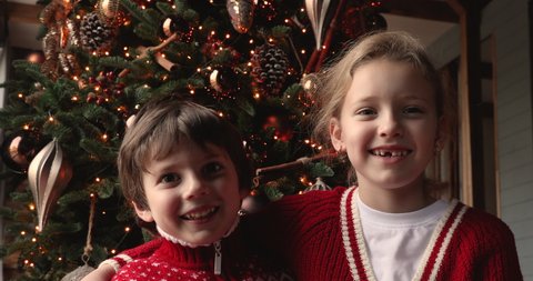 Adorable siblings little girl preschool boy enjoy video call communication with family sit near decorated glowing Christmas tree. Winter holidays congratulation remotely using modern tech app concept