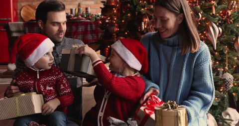 Happy family with little daughter and son in Santa hats gathered together on Christmas morning near xmas tree chatting enjoy gifts opening. New Year celebration, presents store advertisement concept