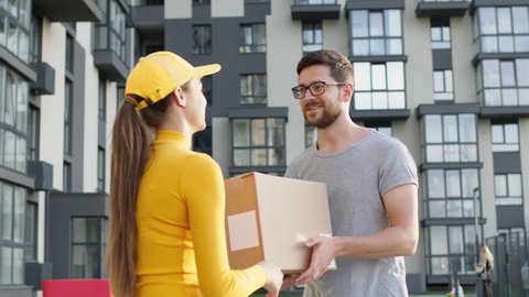 Meeting On The Street Girl Delivery Worker And Customer. Guy Keeps The Received Order In Box. Pretty Girl In Yellow Cap With Long Hair. Takes Box Of Young Guy In Glasses With Beard. He Thanks And