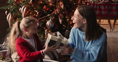 Family sit near glowing xmas tree celebrating New Year, mom giving present to little daughter congratulates her Merry Christmas, kid hug parent express gratitude feels excited. Happy holidays concept