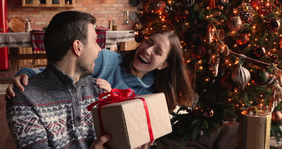 Husband sit with eyes closed receiving giftbox from wife on Christmas Eve, guy feels grateful kisses beloved girl on cheek express gratitude. Best wishes on birthday or xmas, gift store, ideas concept Royalty-Free Stock Footage #1060781056