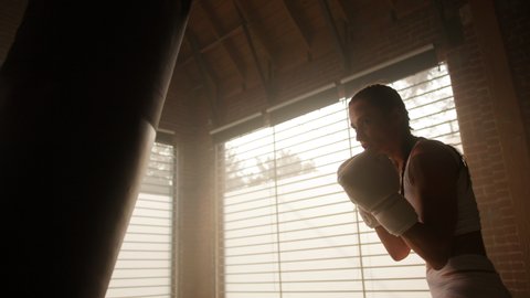 white female athlete boxing the punching bag in urban industrial gym