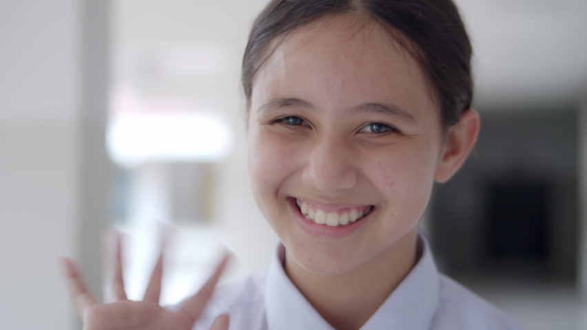 A smiling high school teen girl in white uniform student is greeting by facial expression and waving her hand happily.
