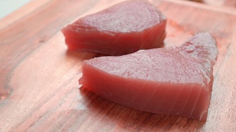 Close-up of Raw Yellowfin Tuna steaks on a wooden cutting board in 4K. Raw Tuna with cooking ingredients on a table, ready for Seared Tuna Dish.