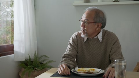 Medium shot : Sad old retired gray haired grandpa asian man sitting alone at table desk at window boring stay home self isolation quarantine feeling depress in problem mental health.