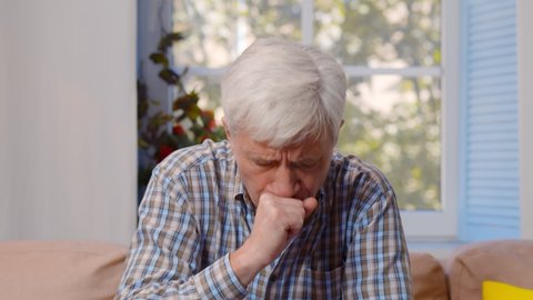 Portrait of old caucasian man getting cold and coughing at home